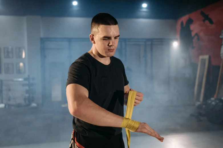 a man in a black shirt holding a yellow tape, inspired by Ma Quan, kickboxing, avatar image, anton fadeev 8 k, indoor picture