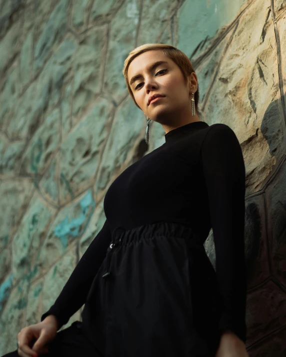 a woman in a black dress leaning against a stone wall, an album cover, inspired by Elsa Bleda, trending on unsplash, realism, wearing a track suit, nonbinary model, asian women, black turtle neck shirt