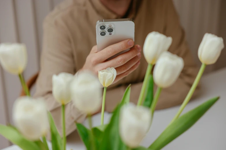 a person sitting at a table using a cell phone, trending on pexels, romanticism, white flowers, who is a male android, with a long white, product introduction photo