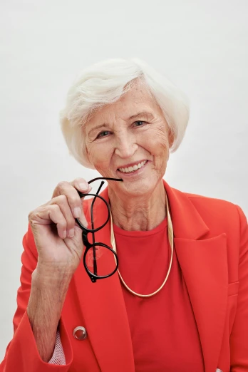 a woman in a red jacket holding a pair of glasses, with short bobbed white hair, zeiss lenses