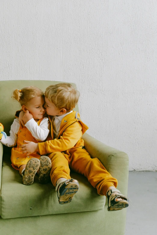 a couple of kids sitting on top of a green chair, pexels contest winner, romanticism, yellow clothes, cuddling, kissing together, couch