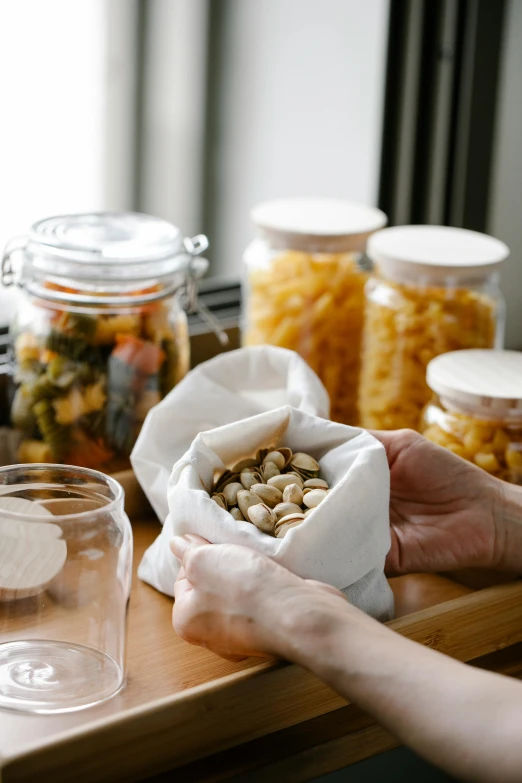 a person holding a bag of food on a table, a still life, by Everett Warner, unsplash, large jars on shelves, nut, buds, cloth wraps