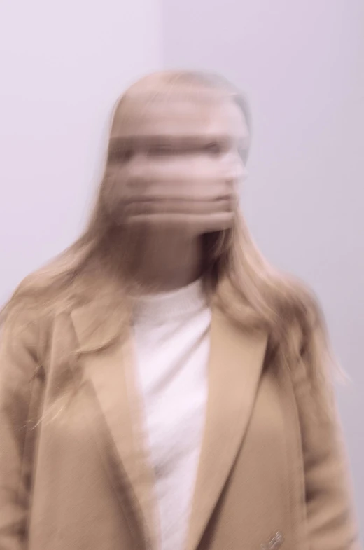 a blurry image of a woman in a beige coat, inspired by Anna Füssli, aestheticism, human head with blonde hair, distorted, photo from a promo shoot, pareidolia