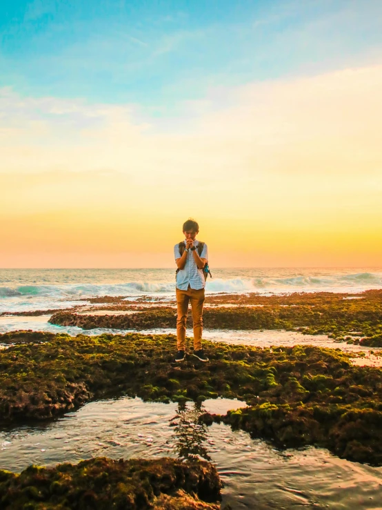 a man standing on top of a beach next to the ocean, rock pools, girl watching sunset, vivid and vibrant, views to the ocean