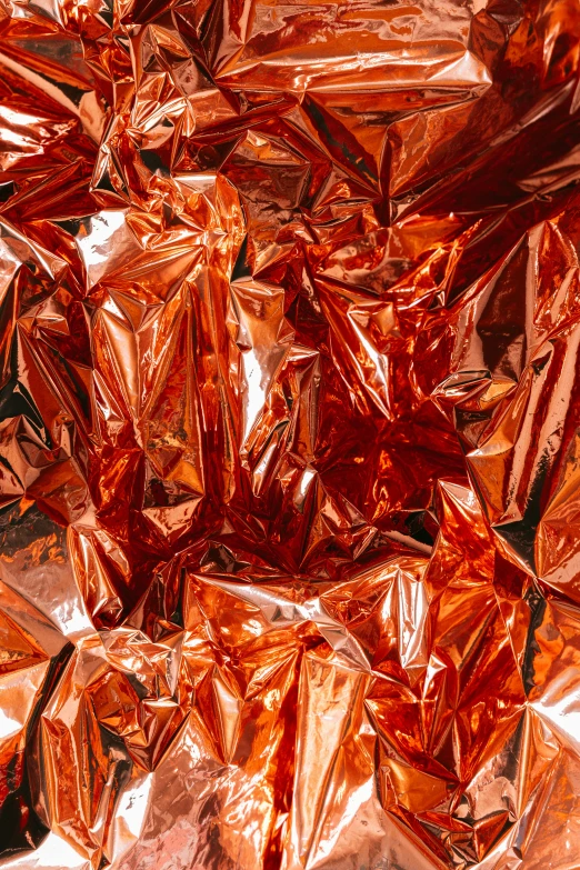 a pile of foil sitting on top of a table, inspired by Christo, pexels contest winner, abstract expressionism, color palette is dark orange, crystal material, rose gold, bright red