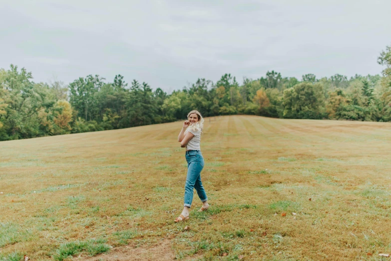 a woman standing on top of a lush green field, by Carey Morris, happening, wearing jeans, sydney sweeney, background image, low quality photo