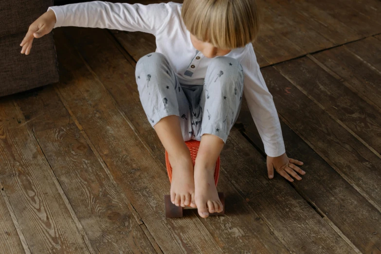 a little girl that is sitting on a skateboard, an album cover, inspired by Sarah Lucas, pexels contest winner, hardwood floor boards, grey orange, thumbnail, small