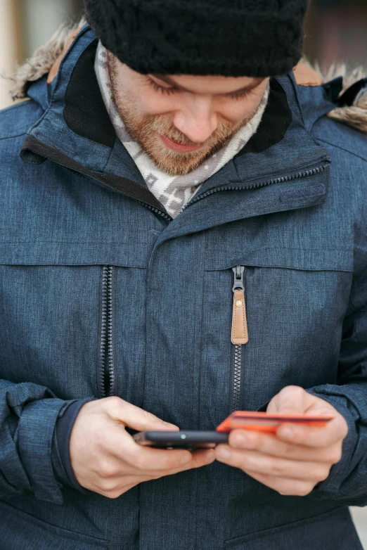 a man is looking at his cell phone, by Jan Tengnagel, happening, blue parka, wearing a jeans jackets, dark grey and orange colours, neck zoomed in