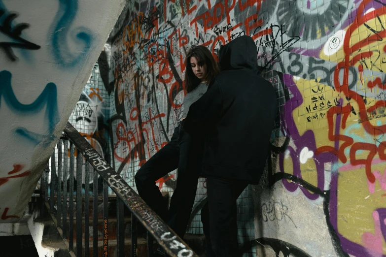 a woman leaning against a wall with graffiti on it, pexels contest winner, man grabbing a womans waist, wearing a dark hood, fighting scene, filmstill