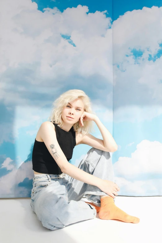 a woman sitting on top of a white floor, an album cover, trending on pexels, realism, tattoos of cumulus clouds, dressed anya taylor - joy, bleached blonde short hair, solid background