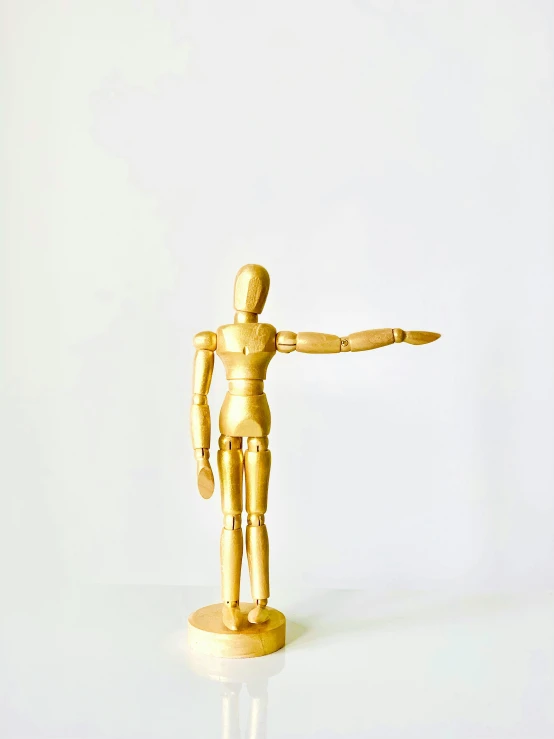a wooden mannequin standing on a white surface, has gold, arms out, 2019 trending photo, 1 figure only