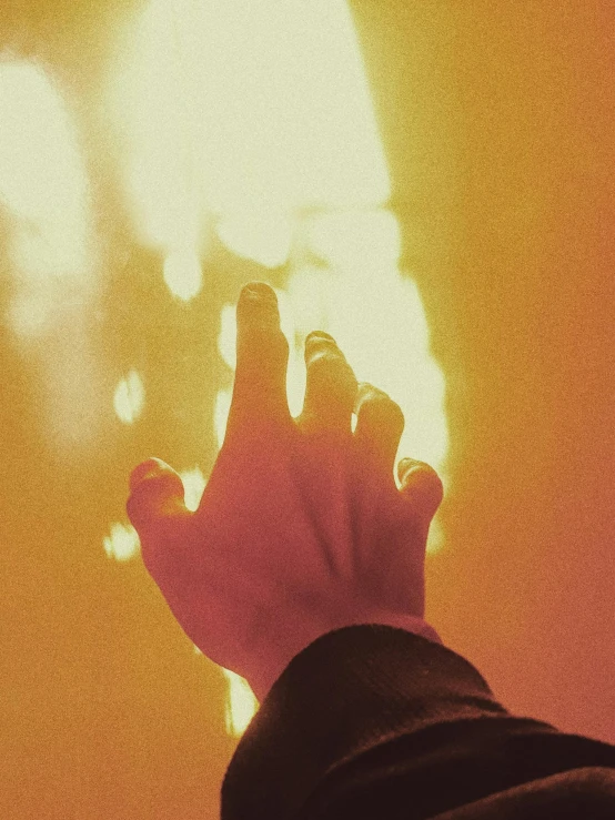 a person holding their hand up in the air, an album cover, inspired by Elsa Bleda, unsplash, synthetism, red and yellow light, holy rays, morning light showing injuries, low quality grainy