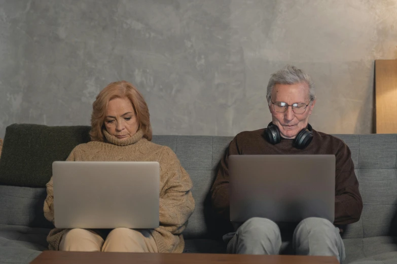 a couple of people sitting on a couch with laptops, trending on pexels, two old people, cyborgs working, brown, evenly lit