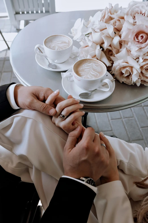 a man and a woman holding hands at a table, a colorized photo, by Emma Andijewska, trending on unsplash, romanticism, celebration of coffee products, luxurious wedding, silver，ivory, a high angle shot