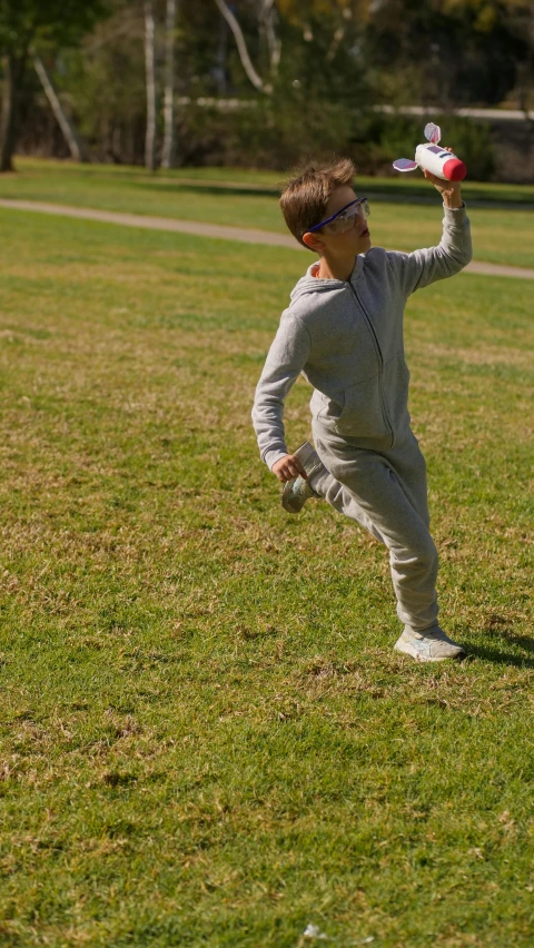 a little boy standing on top of a lush green field, inspired by Liao Chi-chun, pexels, arabesque, wearing a track suit, grey, in an action pose, 15081959 21121991 01012000 4k