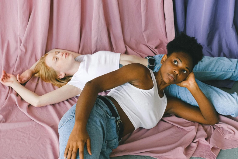 a couple of women laying on top of a pink blanket, by Matija Jama, trending on pexels, renaissance, androgynous person, diverse outfits, wearing a cropped top, on a pale background