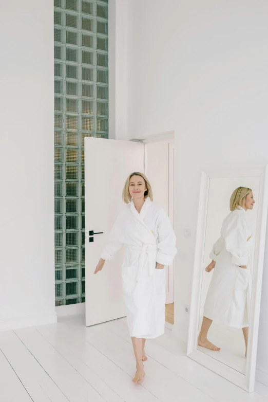 a woman in a bathrobe standing in front of a mirror, in a white room, sydney sweeney, profile image, door