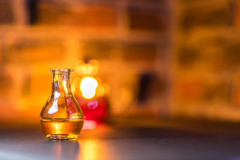 a bottle of liquid sitting on top of a counter, a still life, unsplash, renaissance, candle lights, scientific glassware, warm yellow lighting, alembic