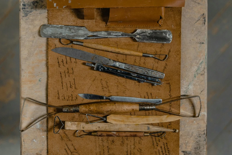 a group of tools sitting on top of a wooden table, a still life, inspired by Joseph Beuys, unsplash, arte povera, engraved blade, surgical impliments, on parchment, on set