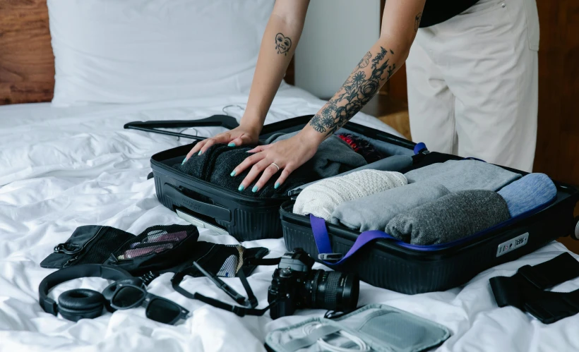 a woman putting clothes in a suitcase on a bed, by Carey Morris, pexels contest winner, with tattoos, carrying survival gear, black and blue and purple scheme, partially cupping her hands