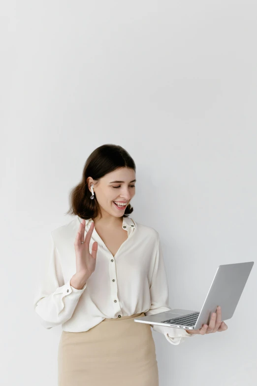 a woman standing in front of a white wall holding a laptop, a cartoon, trending on pexels, renaissance, waving and smiling, working in a call center, wearing white silk, intricate image