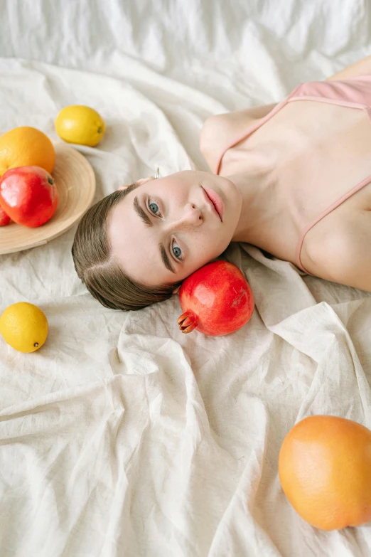 a woman laying on a bed surrounded by fruit, by Eva Frankfurther, unsplash contest winner, natural soft pale skin, red and yellow scheme, headshot photo, on a pale background