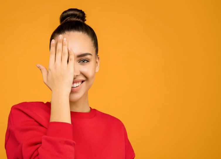 a woman covering her face with her hands, an album cover, shutterstock contest winner, antipodeans, wearing an orange t-shirt, perfect smile vogue, hair styled in a bun, red and yellow color scheme