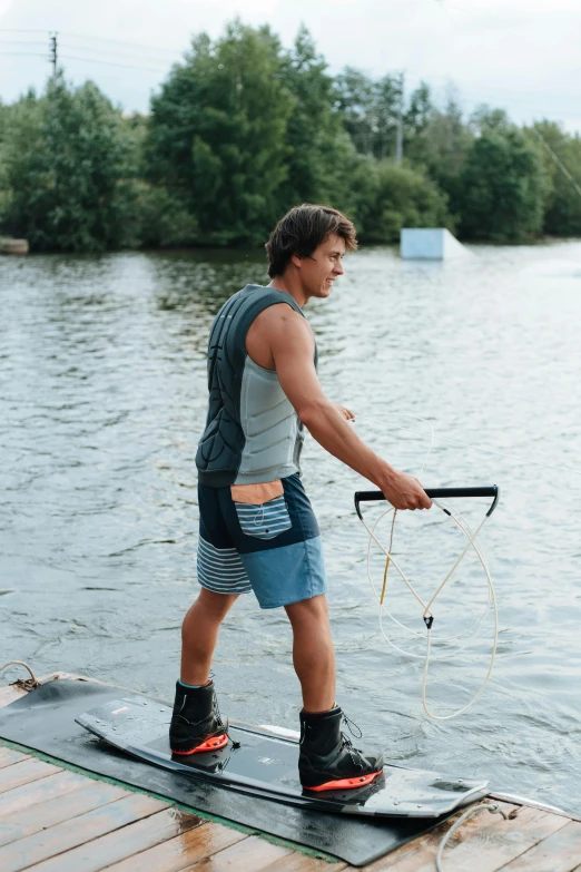 a man riding skis on top of a wooden dock, wearing a tank top and shorts, federation clothing, on a riverbank, body harness