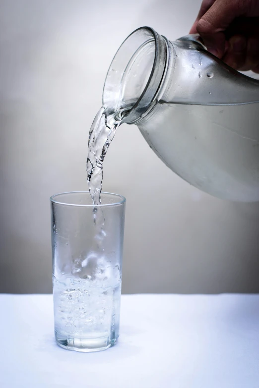 a person pouring water into a glass, large tall, clear, glassware, uncropped