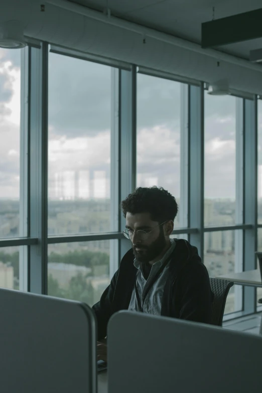 a man sitting at a desk in an office, pexels contest winner, movie still 8 k, skyline showing from the windows, h3h3, programmer