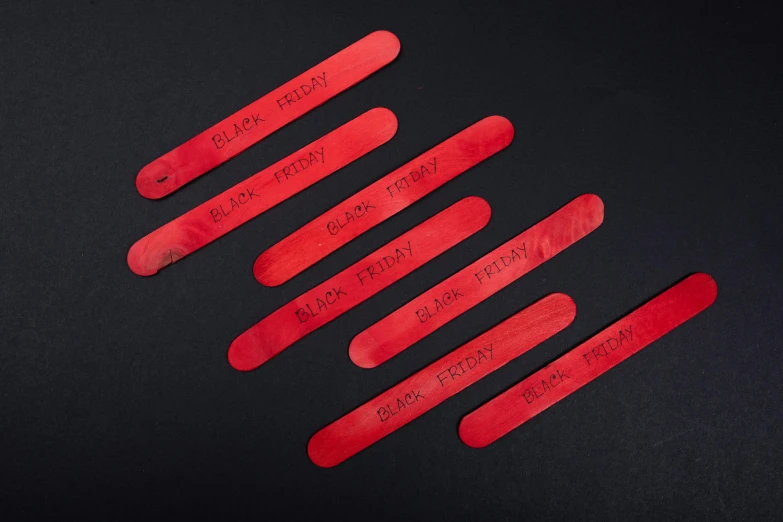 a group of red pops sitting on top of a black surface, engraved blade, wooden art toys, black vertical slatted timber, product shot