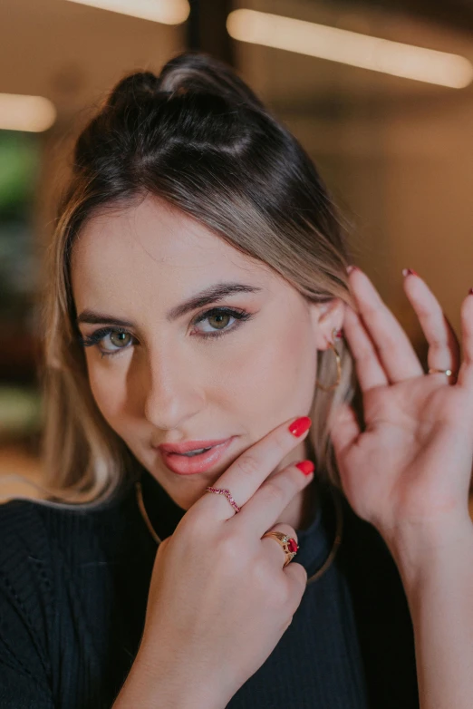 a woman sitting at a table with her hands on her face, a portrait, trending on pexels, earring, in sao paulo, ana de armas, silver gold red details