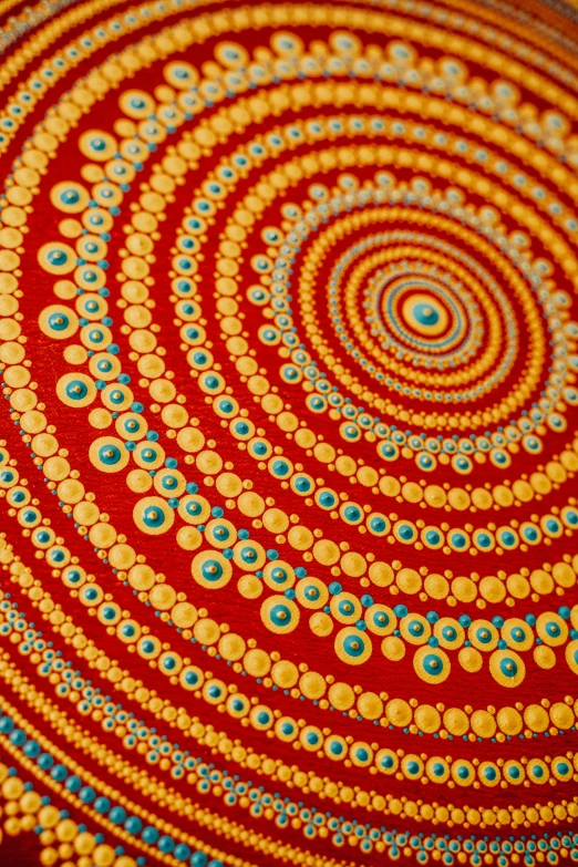 a close up of a painting on a table, by Elizabeth Durack, kinetic pointillism, hindu ornaments, red and yellow, spiral, cotton