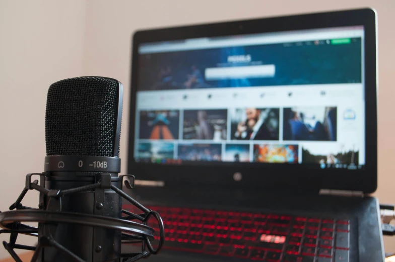 a laptop computer sitting on top of a desk next to a microphone, pexels, video art, gaming pc, looking towards camera, album cover, banner