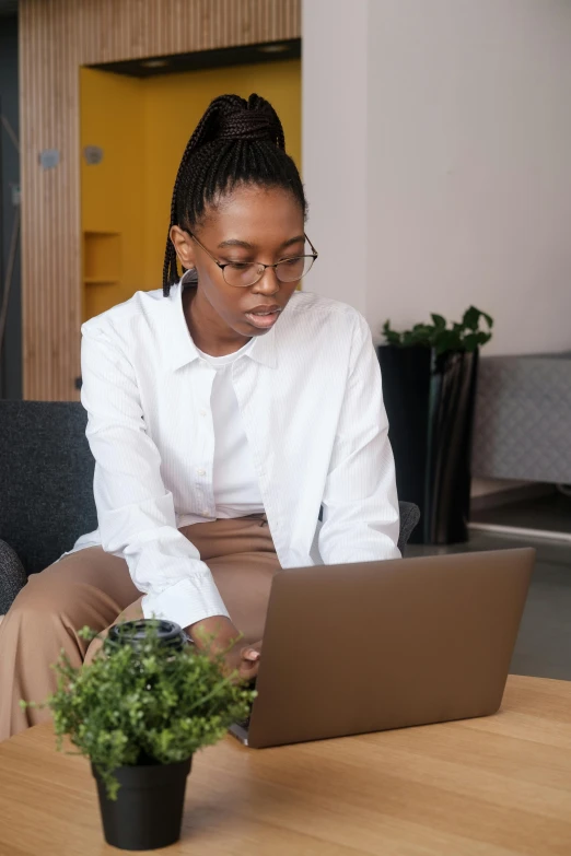 a woman sitting on a couch using a laptop, trending on pexels, renaissance, wearing white suit and glasses, black female, white shirt and green skirt, tech demo