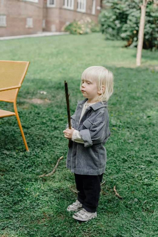 a little boy standing on top of a lush green field, an album cover, pexels contest winner, holding the elder wand, sitting in the garden, grey, fire staff