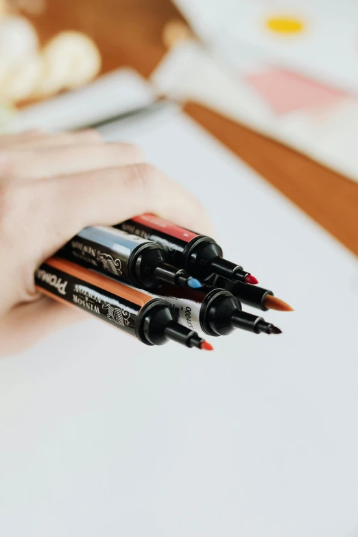 a person that is holding some pens in their hand, detailed product image, black and orange colour palette, coloured marker, product shot