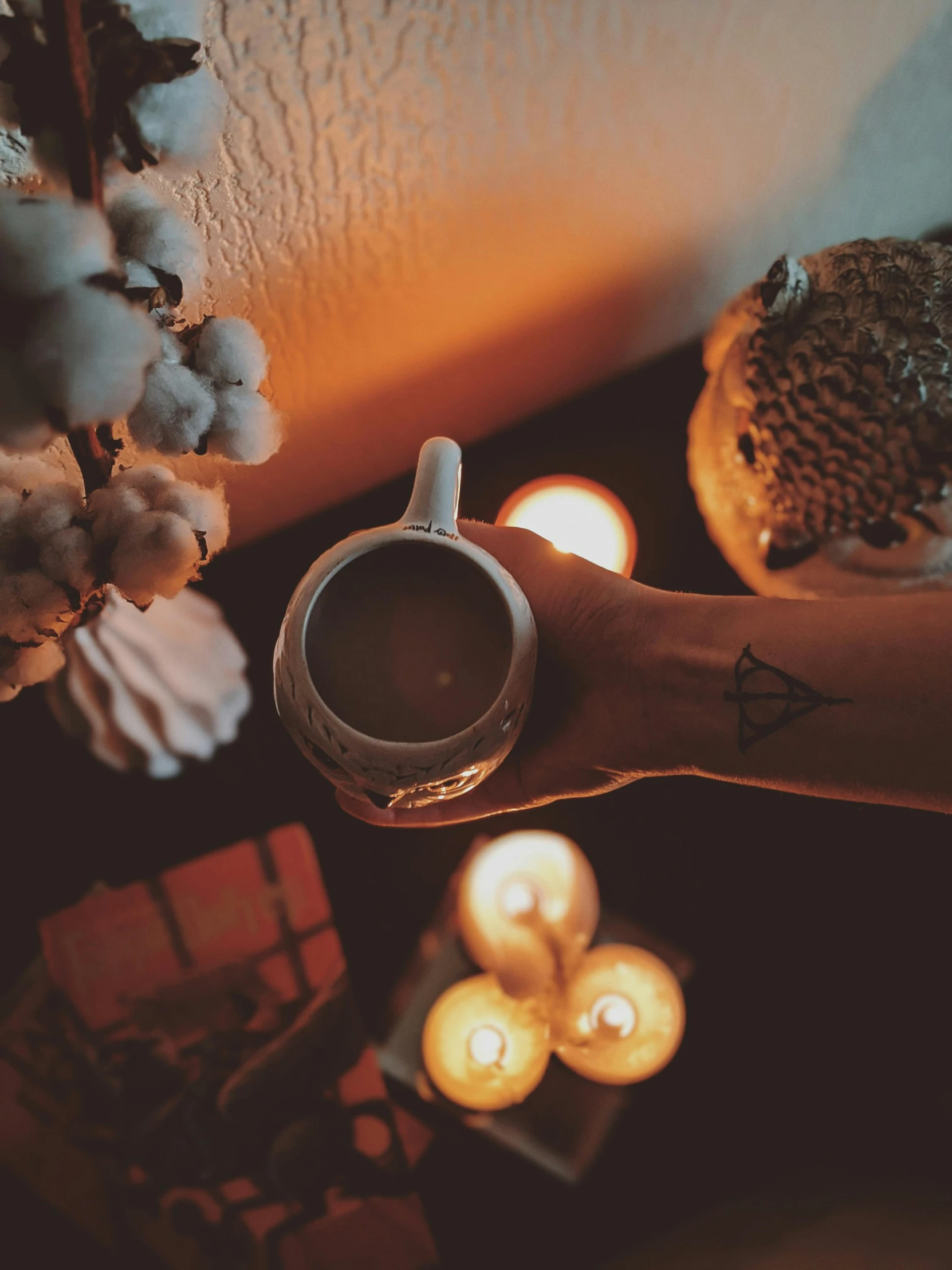 a person holding a cup of coffee next to some candles, a tattoo, inspired by Elsa Bleda, trending on pexels, aestheticism, 8k octan photo, ☁🌪🌙👩🏾, home wicca scene, (1 as december