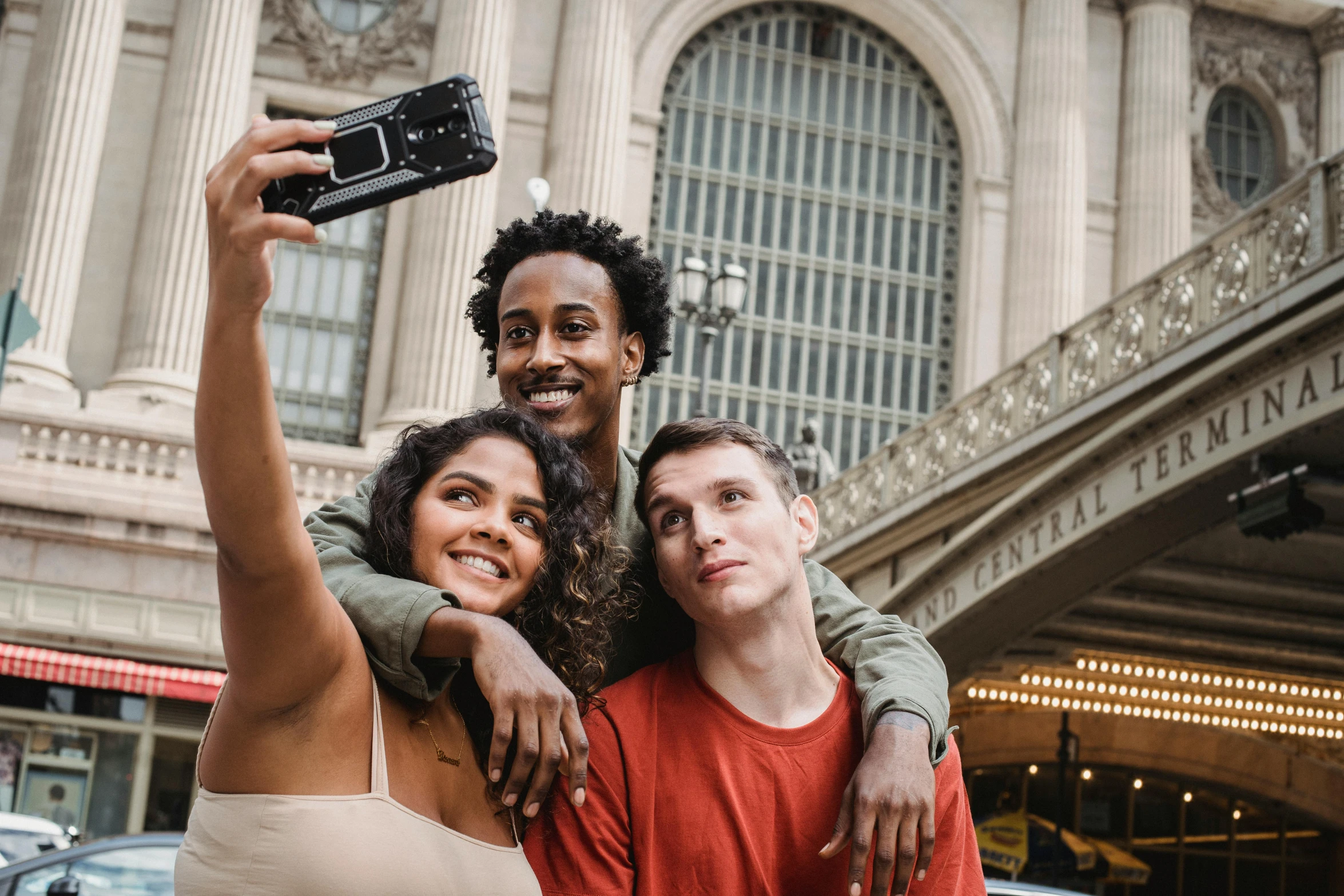 three people taking a selfie in front of a building, pexels contest winner, central station in sydney, in the middle of new york, diverse, promotional image