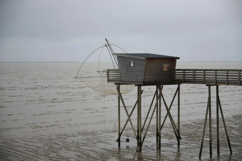 a fishing net sitting on top of a wooden pier, houses on stilts, slide show, grey sky, water levels