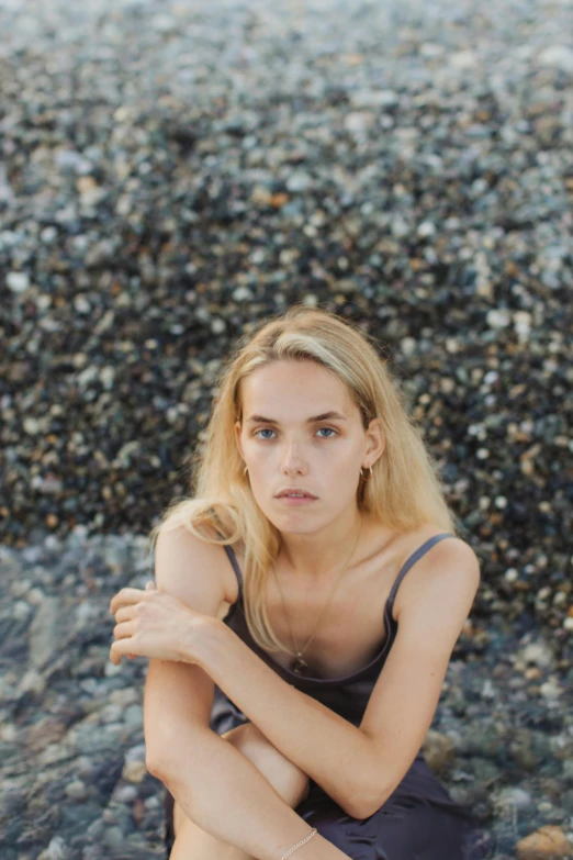 a woman sitting on top of a rocky beach, a portrait, by Sara Saftleven, unsplash contest winner, with high cheekbones, greasy hair, young blonde woman, 15081959 21121991 01012000 4k