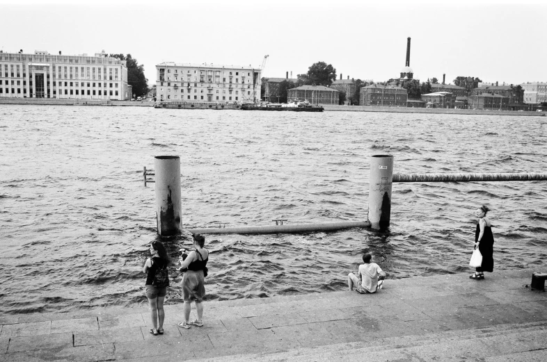 a group of people standing next to a body of water, a black and white photo, inspired by Henri Cartier-Bresson, fluxus, saint petersburg, hot summer day, medium format film photography, fallen columns