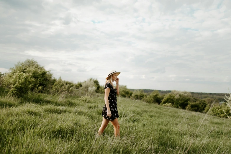 a woman standing on top of a lush green field, unsplash, wearing black dress and hat, wearing in a summer dress, people walking around, patterned clothing