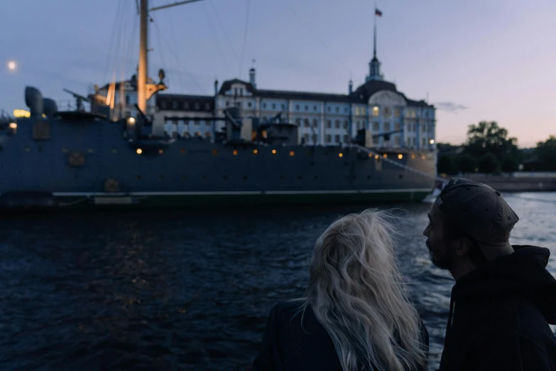 a man and a woman standing in front of a boat, by Jesper Knudsen, pexels contest winner, happening, submarine in background. dark, late summer evening, viewed from the harbor, music video