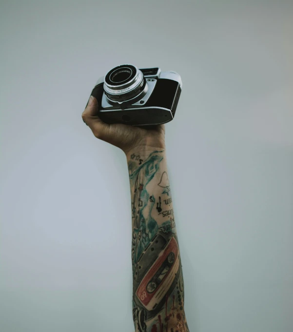 a person holding a camera in their hand, a tattoo, on a pale background, photography], photography ), jay bauman