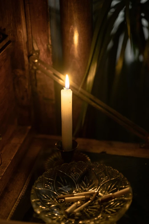 a lit candle sitting on top of a glass plate, in a dark dusty parlor, light inside the hut, gothic lighting, soft lighting from above