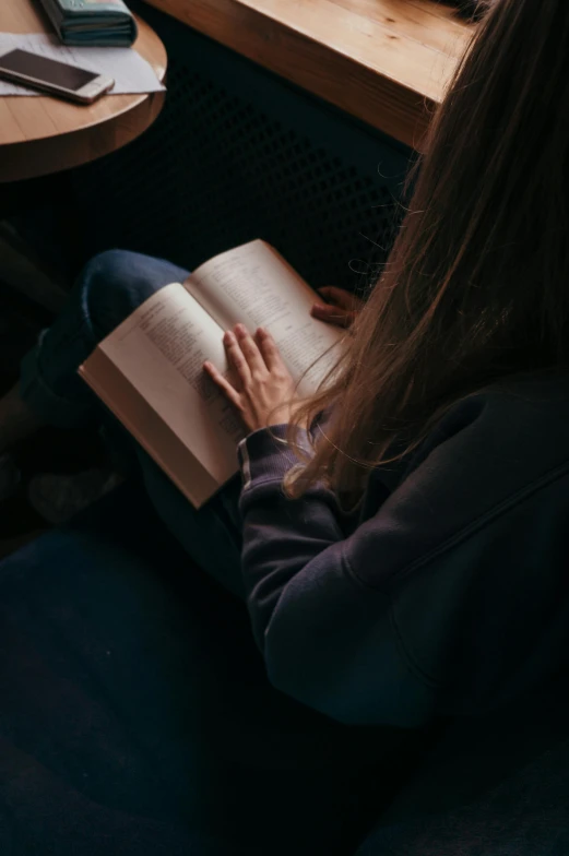 a woman sitting on a couch reading a book, inspired by Elsa Bleda, pexels contest winner, renaissance, wearing a dark shirt and jeans, moody dim faint lighting, hands straight down, schools