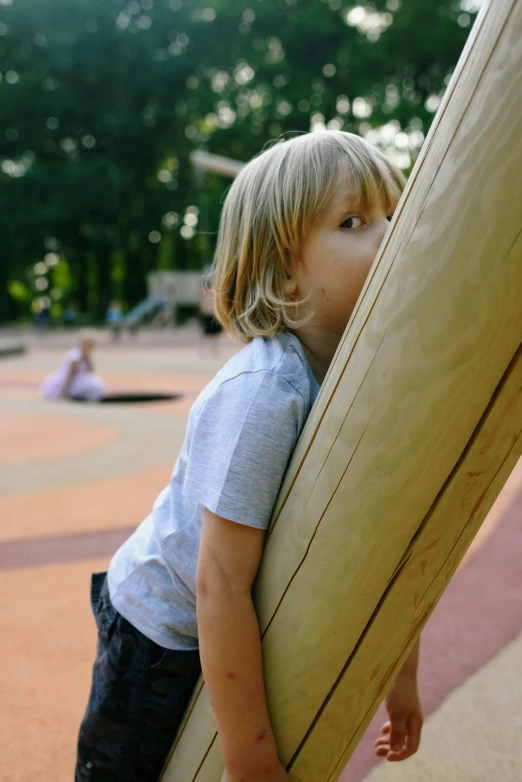 a little boy that is holding a surfboard, inspired by Jan Rustem, unsplash, conceptual art, playground, massive wide trunk, cardboard, concerned