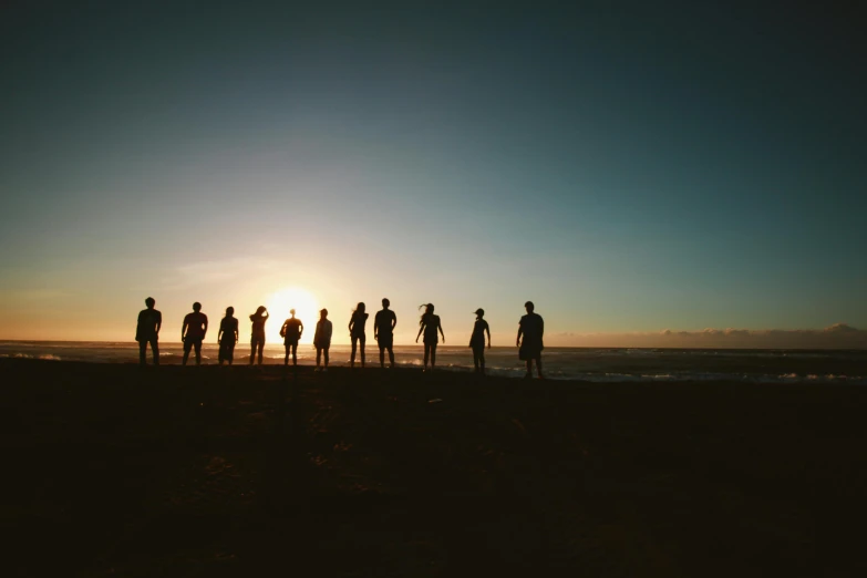 a group of people standing on top of a beach, pexels contest winner, back lit, lined up horizontally, 12 figures, teams