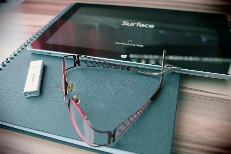 a tablet computer sitting on top of a notebook, square rimmed glasses, surface imperfections, thumbnail, subsurface